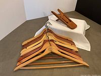 Seven wooden clothes hangers with natural and darker wood finishes, some with metal hooks.