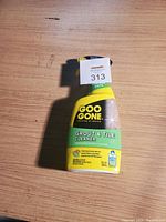 Front view of a yellow and green plastic spray bottle labeled Goo Gone Grout & Tile Cleaner on a wood surface.