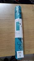 Rolled teal Jogi yoga mat wrapped in plastic with visible product label and branding.