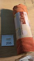 Photo of rolled orange Gaiam Sol Thirsty Towel mat with packaging label and MaxSold lot card beside it, showing the towel material texture and color.