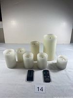 Two sets of white battery operated candles with remote controls placed on white background.