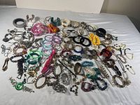 Full overview of the jewelry lot showing many bracelets and jewelry pieces laid out on white fabric.
