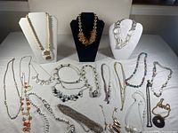 Full overview of costume jewellery lot featuring multiple necklaces and bracelets draped and laid flat on white background. Includes items on three display busts and scattered items.