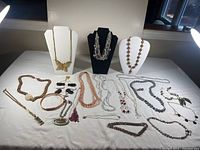 Photo showing an assortment of costume necklaces and bracelets in various styles and colors, some on display busts and some laid flat on a white surface.