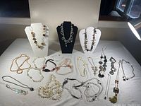 Complete view of multiple costume necklaces laid out with three displayed on bust stands showing varied necklace styles including beaded, linked, and pearl-like designs.