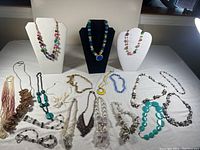 Overall assortment of costume necklaces displayed on three necklace busts and laid flat on a table showing the variety and condition of pieces.