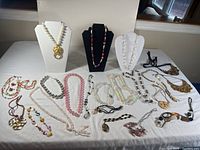 Wide view of entire lot showing various costume necklaces arranged on a white cloth, including some displayed on necklace busts