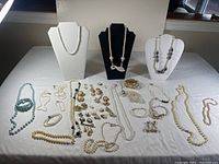 Full overview of the lot with various pearl necklaces, bracelets, earrings, and brooches arranged on a white cloth with three display busts showing necklaces.