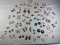Overview of many pairs of earrings on white background, different styles and colors visible.