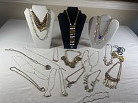 Full view of 20 pieces of gold-tone costume jewelry spread out and displayed on necklace stands and flat surface.