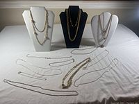 Full view of all 14 gold-tone costume jewellery pieces including necklaces displayed on necklace stands and laid flat