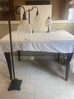 Full view of all three lamps on a dining table with white cloth, showing floor lamp, square table lamp, and round table lamp.