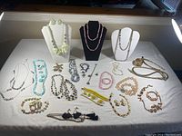 Full overview of assorted costume jewelry sets displayed on white surface, including necklaces on bust stands.