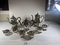 Front view showing two silver coffee pots, one tea pot, and three cream and sugar sets with visible stains.