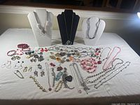 Full view of assorted Valentine-themed costume jewelry including necklaces on bust stands, bracelets, earrings, and pins laid out on white cloth.