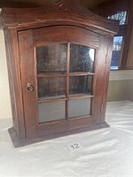 Front view showing the wooden cabinet with glass pane door and metal ring pull handle.