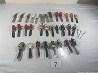 Full collection of 34 vintage cheese spreaders displaying decorative holiday and character handles in rows on white surface.