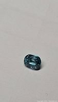 Close-up photo of the oval cut lagoon blue Cambodian zircon gemstone showing facets and clarity on a white background.