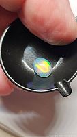 Close-up image of a single oval cabochon Ethiopian opal, showing its size comparison with fingertip and vibrant play of colors under light.