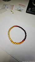 Top view of the amber bracelet showing the gradient of beads from light yellow to dark amber tones on a white background.