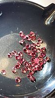 Close-up photo showing multiple small round brilliant-cut hot pink sapphire gemstones gathered together in a dark, shallow dish for display.
