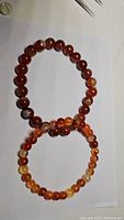 Two red agate bead bracelets lying flat on a white surface, one with larger beads (8mm) and one with smaller beads (6mm). Both bracelets have natural color variations and patterns in the beads.