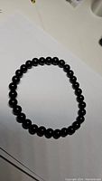 Single strand bracelet made of round, polished black onyx beads, laid flat in a circular shape.