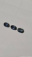 Three oval cut sapphires arranged in a row showing color and facets under lighting.