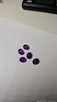 Top view of five deep purple amethyst cabochon gemstones arranged on white paper.