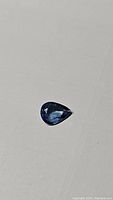 Clear image of pear cut natural denim blue sapphire gemstone on white background, showing faceting and color variation.