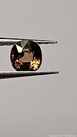 Close-up image of the cushion cut tourmaline held by tweezers showing the stone's color and clarity.