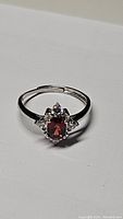 Front view of the sterling silver ring showing the oval cherry red garnet and small clear accent stones.