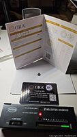 Photo of the GRA certificate booklet, moissanite stone, warranty card, and diamond tester device showing the authenticity check.