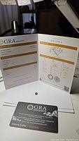 GRA certification report opened showing grading details and moissanite placed beside it, with GRA card visible.