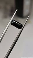 Close-up image showing rectangular octagon cut green tourmaline gemstone held by tweezers, highlighting cut and clarity.