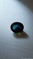 Photo showing oval cut teal sapphire gemstone with visible facets and rich blue-green color under direct light.