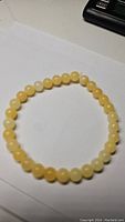 Photo showing a circular stretchy bracelet made of polished round honey calcite beads laid flat on a white surface.