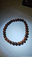 Full view of the Mahogany Jasper beaded stretchy bracelet laid out in a circle on a white surface, showing consistent bead size and color pattern.