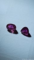 Two pink sapphire gemstones on a white surface showing inclusions and blue splotches.