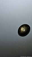 Oval cabochon black star sapphire placed on a reflective surface showing a six-ray star flash under light.