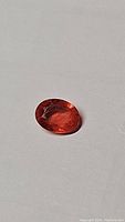Photo of oval cut orange-pink sapphire gemstone on plain background showing color and faceting.