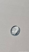 Oval cut faceted blue aquamarine gemstone on a plain surface, visible clarity and color tone.