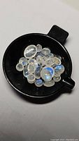 Lot of mixed cabochon cut rainbow moonstone stones with blue flash in black measuring tray.