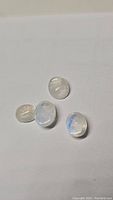 Four oval cabochon rainbow moonstone gemstones displaying blue flash and natural inclusions on a plain white background.