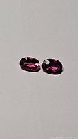 Pair of oval cut bright pink umbalite garnet gemstones on a plain background showing color and clarity.