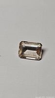Topaz gemstone from a distance showing emerald cut and soft champagne color on a light background.