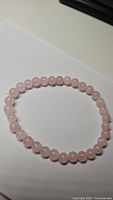 Photo of a natural rose quartz bead bracelet laid flat on a white surface under ambient light.