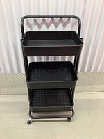 Front view of 3 level wheeled cart showing all three black perforated trays, metal frame, and wheels.