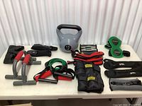 Full view of all exercise items on table including kettlebell, wrist weights, ankle weights, push-up bars, resistance bands.