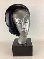 Front view of the painted bronze sculpture showing stylized female head in silver and black on wooden base